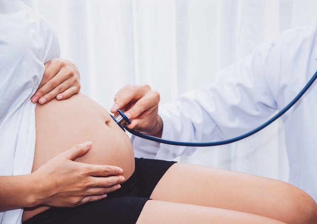 Il medico sta controllando la donna incinta con lo stetoscopio nel concetto di assistenza sanitaria dell'ospedale