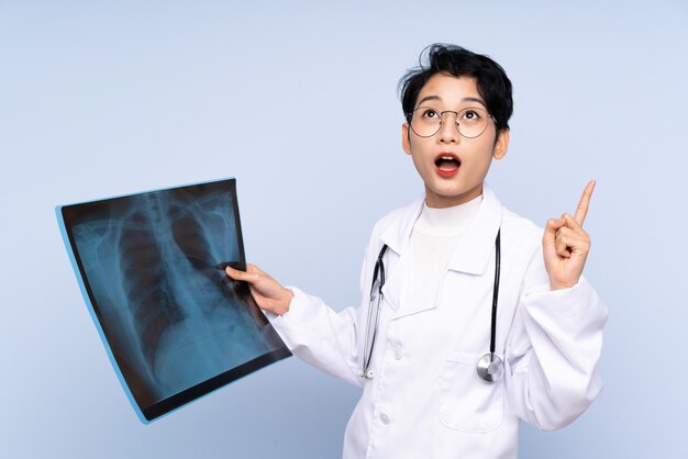 Женщина доктора азиатская держа сканирование кости над изолированной голубой стеной
