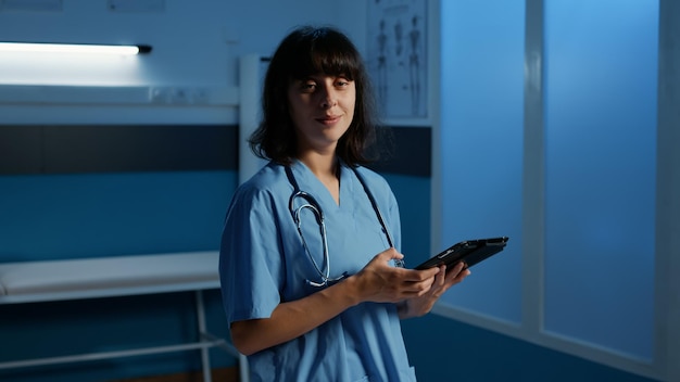 Doctor assistant in medical uniform typing health care\
treatment on tablet computer during checkup visit appointment in\
hospital office late at night.tired nurse working in clinic after\
hours