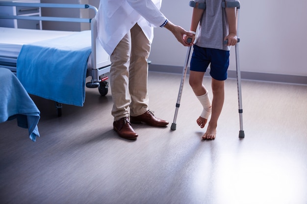 Doctor assisting injured boy to walk with crutches