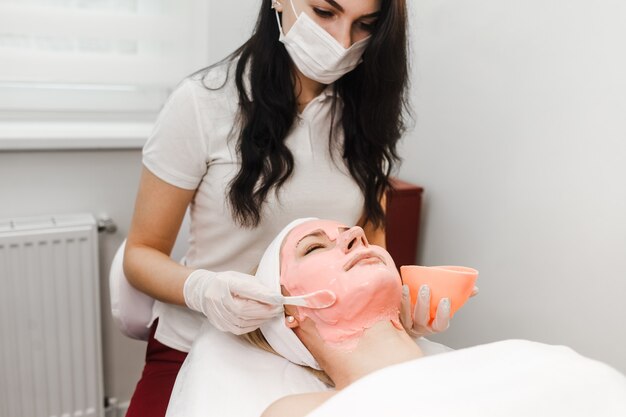 Foto medico estetista applica una maschera antietà sul viso della donna.