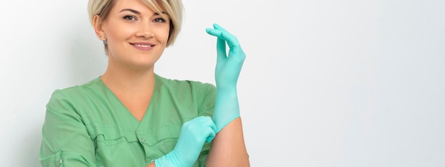 医師の美容師は、笑顔で滅菌された青い手袋を着用し、白でクライアントを受け入れる準備をします。