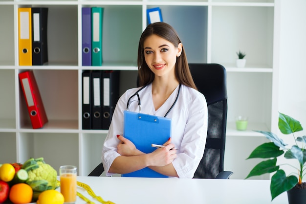 Foto il medico inizia a scrivere un piano di dieta. il bello giovane dietista sorride e lavora nell'ufficio leggero e moderno.