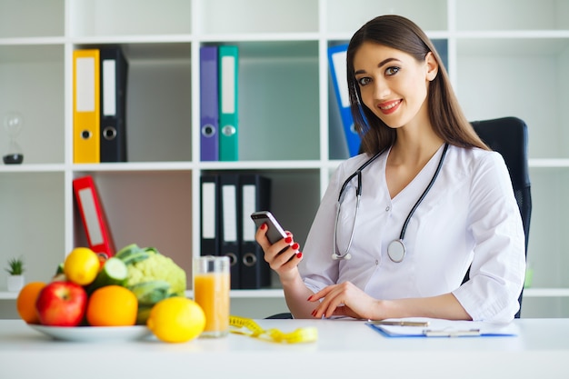 The doctor begins to write a diet plan. beautiful young dietitian smiles and works in light and modern office