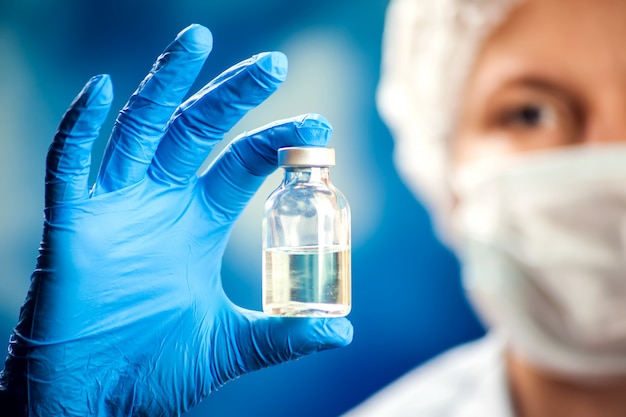 A doctor in blue gloves holding a bottle with vaccine. Close up shot. Medicine and healthcare concept