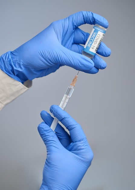 A doctor in blue gloves holds a syringe and an ampule with a vaccine