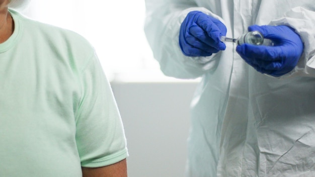 Foto il dottore in guanti di lattice blu riempie la siringa con la medicina dalla fiala di vetro per l'iniezione di una persona anziana in laboratorio medico contro il coronavirus, l'influenza, la malattia del morbillo