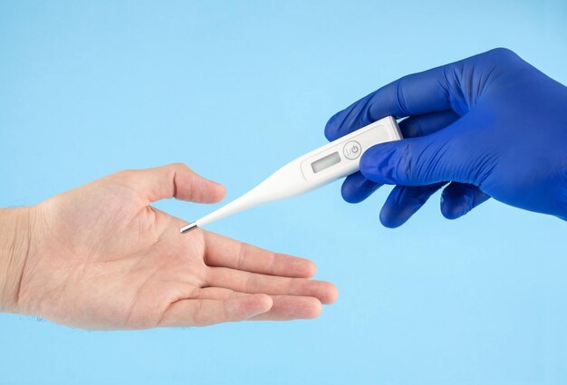 Врач в синих латексных перчатках передает цифровой термометр в руки пациента