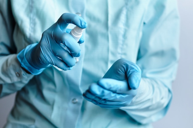 A doctor in blue medical gloves holds an antiseptic sanitizer and sprays on his hands - concept of protection against coronavirus COVID-19.