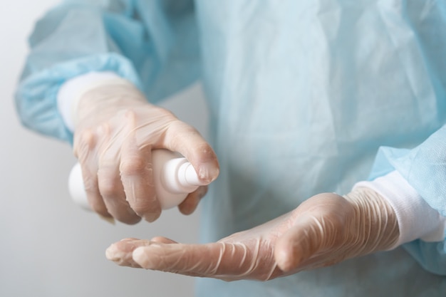 a doctor in a blue medical gown and gloves treats his hands with antiseptic