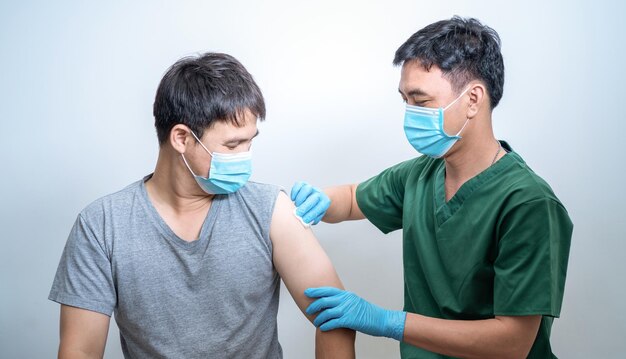 Врач в защитных перчатках СИЗ из синего щебня накладывает хлопковый пластырь на руку до и после инъекции вакцины COVID'19 CORONA