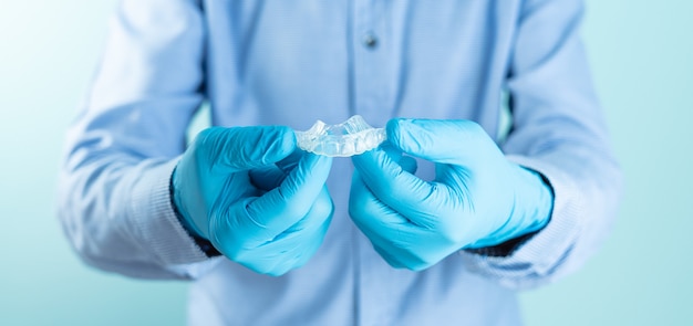 Doctor in blue shirt and gloves showing a transparent dental splint.