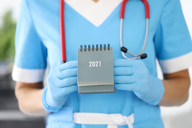 Doctor in blue suit and glove hold calendar.