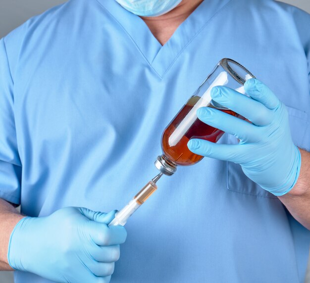  doctor in blue uniform holds a syringe and a glass bottle with injection