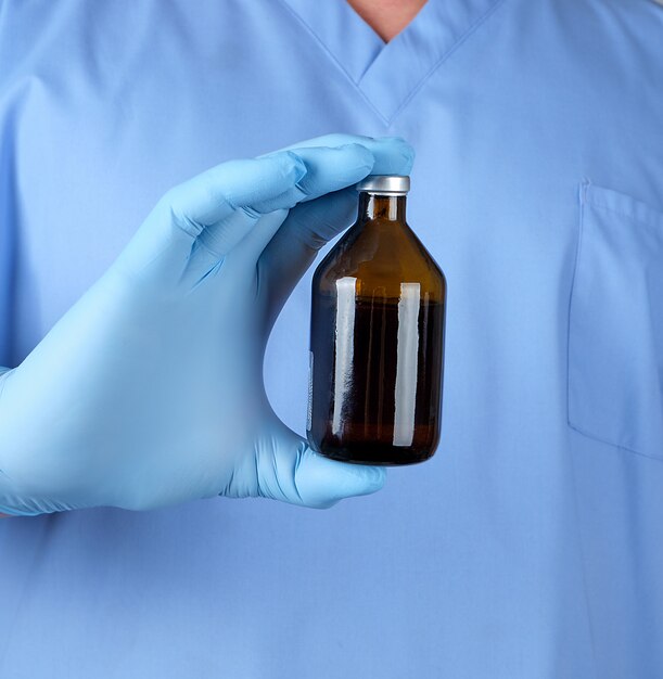 Doctor in blue uniform and latex gloves holding a brown glass bottle with medicine for treatment