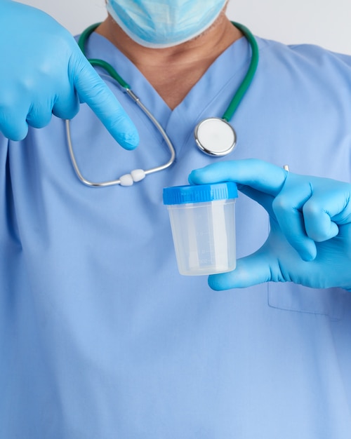 파란색 유니폼과 라텍스 장갑에 의사가 소변 샘플을 채취하기 위해 빈 플라스틱 용기를 들고있다