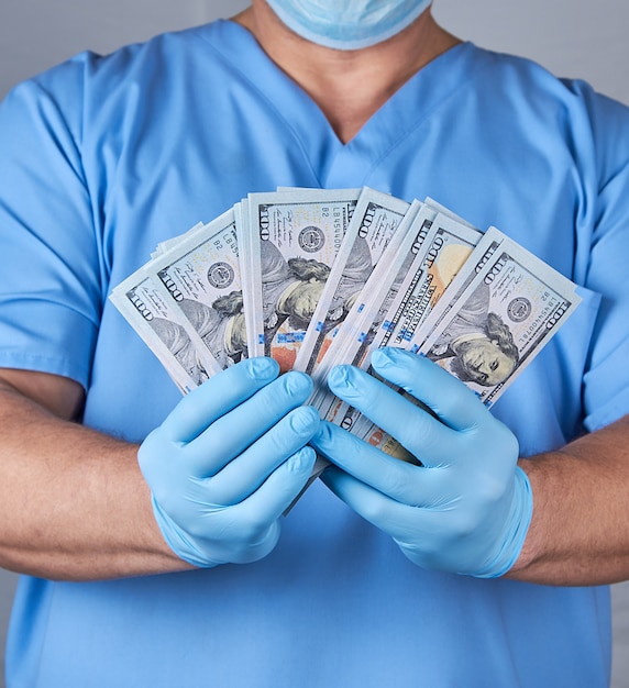 Doctor in blue uniform and latex sterile gloves holds a lot of paper money