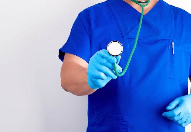 Medico in uniforme blu e guanti sterili in possesso di uno stetoscopio medico