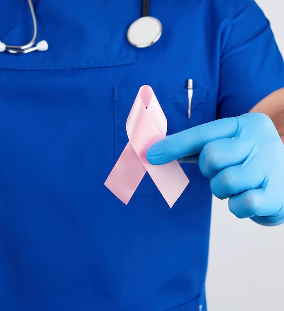 Doctor in blue uniform and sterile latex gloves holds a pink ribbon