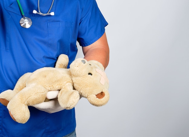 Doctor in blue uniform and white latex gloves holding a brown teddy bear