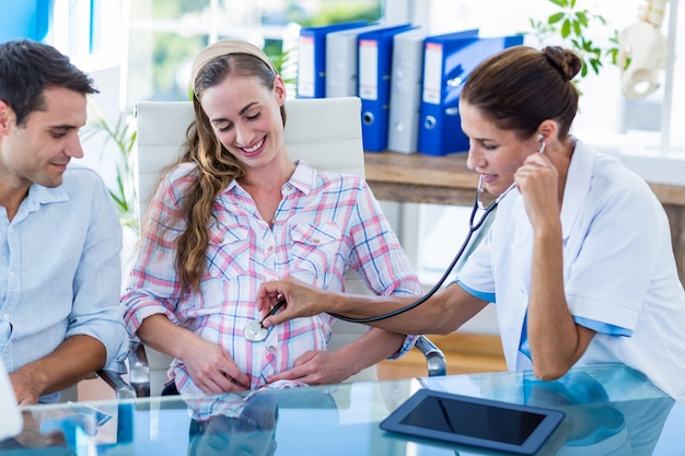 Foto medico che controlla la pancia della donna incinta con lo stetoscopio