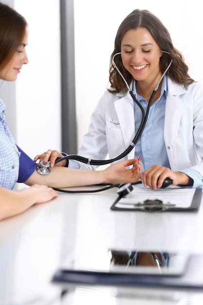 Doctor checking blood pressure of female patient while sitting at the desk in hospital office. cardiology in medicine and health care concept