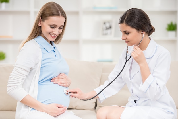 Doctor checking pregnant woman tummy with stethoscope.