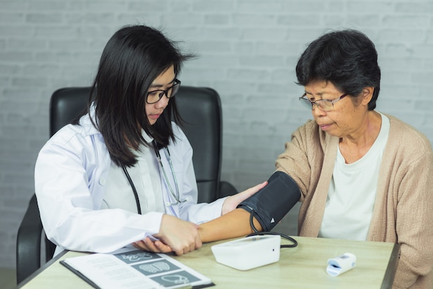 Doctor checking pressure old woman on gray