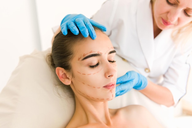 Doctor checking woman's skin before plastic surgery. Surgeon or beautician hands touching woman face.