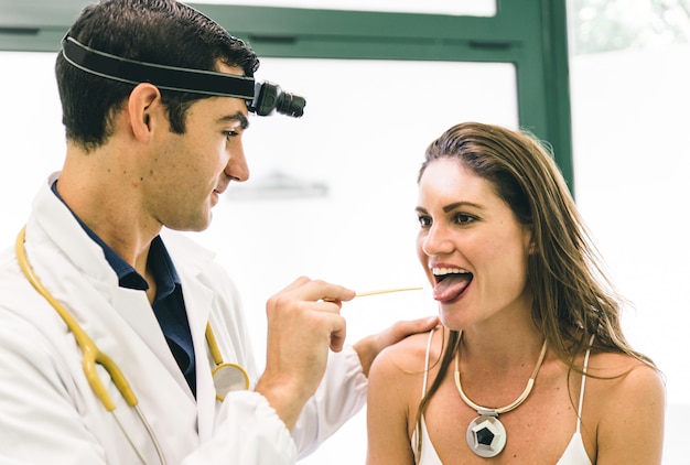 Doctor checking woman throat with the medical stick