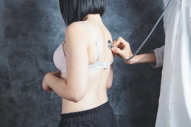 The doctor checks the lungs of a woman in a bra with a stethoscope