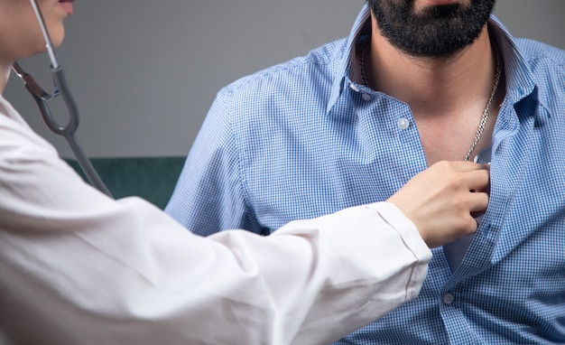 A doctor checks a man's heart with a stethoscope on the sofa