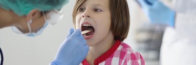 The doctor in the clinic looks at the throat of a girl