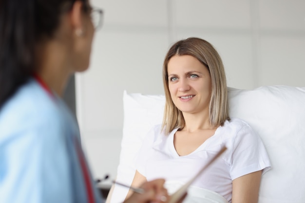 Doctor communicates with bedridden patient in hospital ward medical services concept