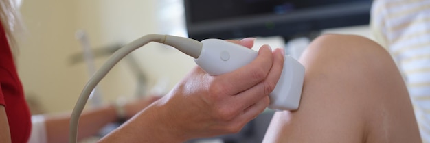 Doctor conducting ultrasound examination of patient knee joint in clinic closeup diagnostics of