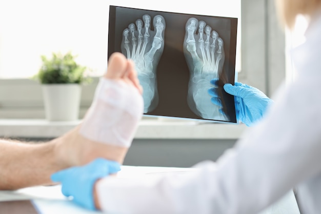 Doctor conducts physical examination of patient with bandaged leg and examines xray image