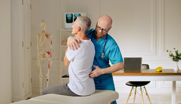 A doctor conducts a physiotherapy session after a medical trauma with a man in the modern rehabilita...