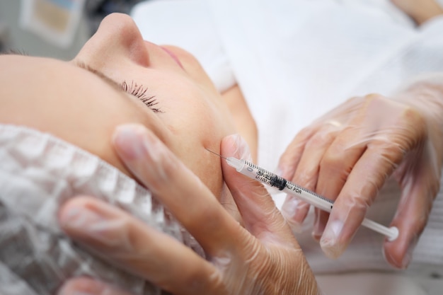 Doctor-cosmetician adds missing volume to cheekbones injecting gel-like medicine under skin selective focus