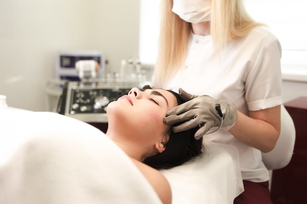 Doctor cosmetologist does facial massage to the patient with electric gloves