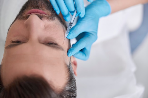 doctor cosmetologist does filler injection to remove crows feet to middle aged man in beauty