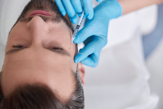 Фото Врач косметолог делает инъекцию филлера для удаления гусиных лапок мужчине средних лет в красоте