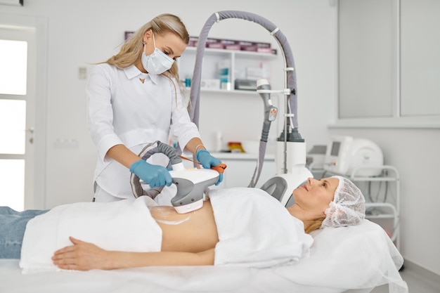 Doctor cosmetologist doing vacuum massage procedure on woman belly