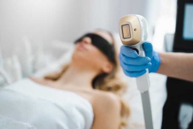 Врач-косметолог держит в руке устройство для лазерной эпиляции