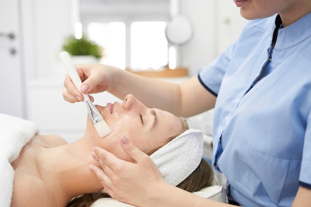 Doctor cosmetologist makes a multistage facial cleansing procedure to a young attractive woman in a beauty salon Summer skin care