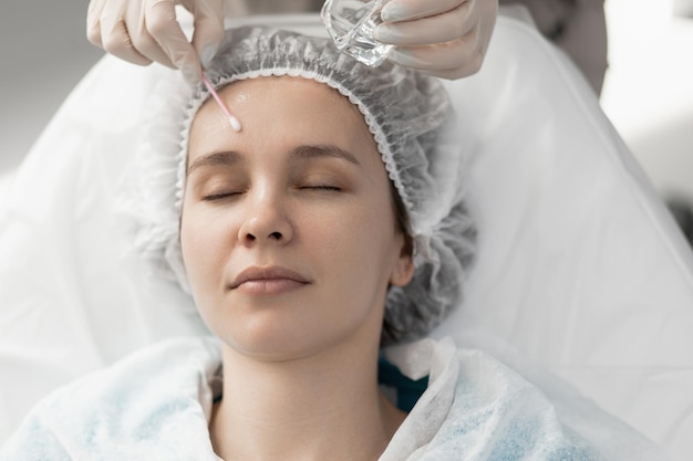 Doctor cosmetologist makes a procedure with a cotton swab on the client's face