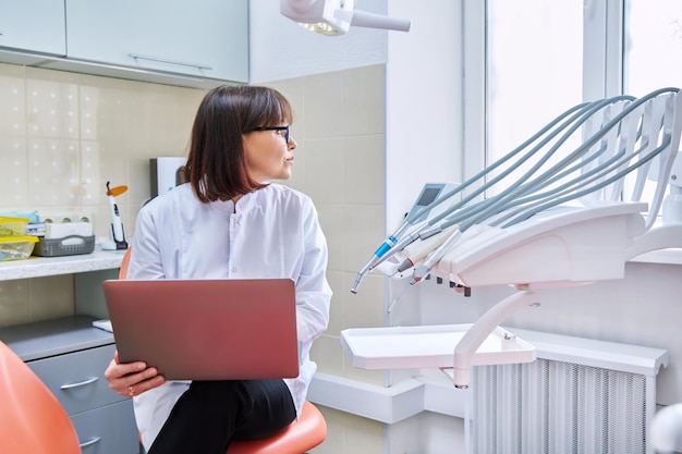 Photo doctor dentist sitting in the office using a laptop dentistry health care treatment work profession medicine concept