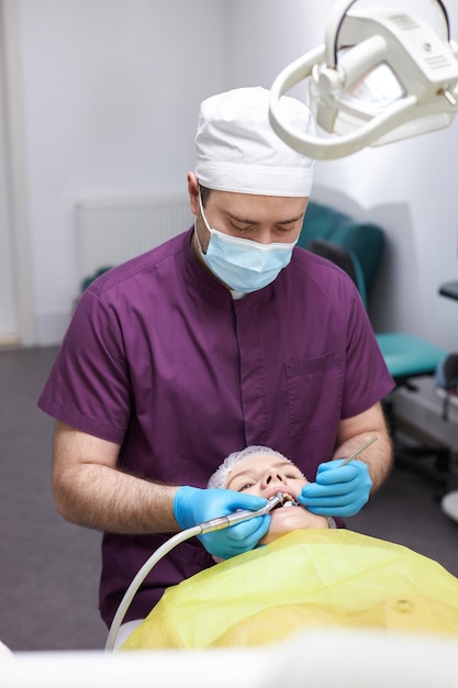 Doctor dentist using dental drill treating decay or caries of woman's teeth in dentistry clinic