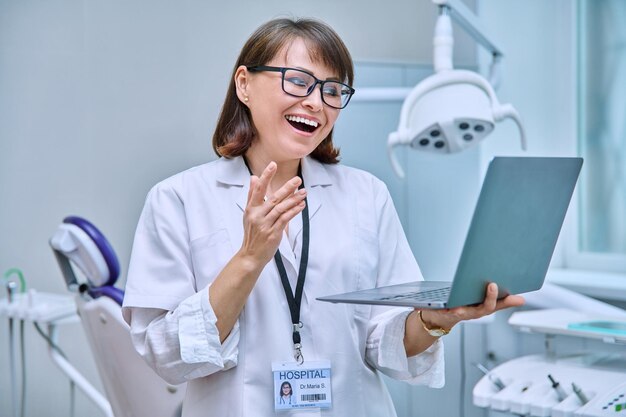 Foto dottore dentista che lavora in ufficio usando il clipboard del portatile che fa videoconferenze, parla, consulta i pazienti online, tecnologia, medicina, odontoiatria, concetto di assistenza sanitaria dentale