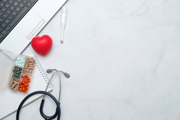 Doctor desk table with stethoscope, medicine, notebook, office supplies.