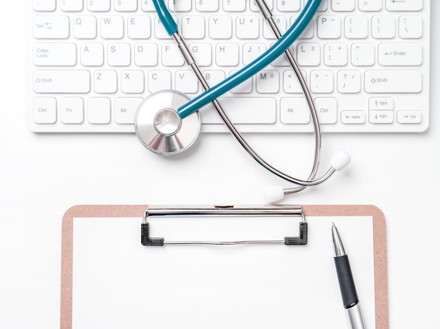 医師は、医療記録ケースと白い作業テーブル上のペンを備えたコンピューターのキーボードで概念聴診器を診断します上面図フラットレイコピースペース